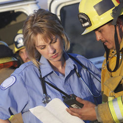 Emergency medical service employee conferring with a firefighter