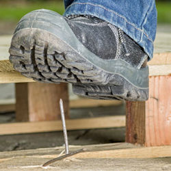 Image of worker wearing work boot about to step on a nail