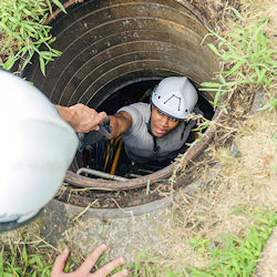 Worker in manhole climbing up ladder.