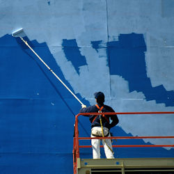 Worker painting over elevated billboard with guardrail system and fall protection.