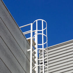 A fixed ladder with cage located outside on the side of a building.