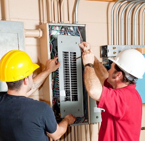 Two electricians working on an electrical panel.