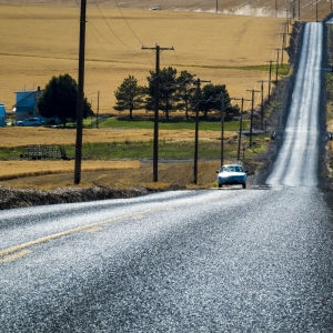 Picture of a single car traveling a long rural road.