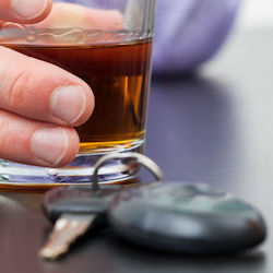 A glass of an alcoholic beverage with keys in the foreground; representing drunk driving.