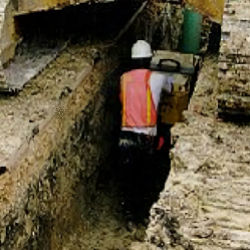 Worker in trench with heavy equipment overhead. Workers must be protected in these situations