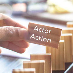 a hand holding a wooden domino with the the words Actor and Action on it.