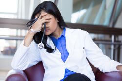 stressed doctor with hand covering face