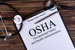 Clipboard with titled OSHA Occupational Safety and Health Administration. There is a stethoscope
                                        in the upper left corner and and magnifiying glass in the upper right corner