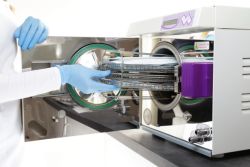 medical worker placing tray of surgical equipment into a sterilizer