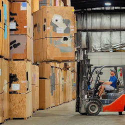 Forklift with driver surrounded by large boxes in a warehouse