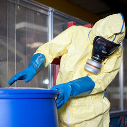 Worker in full PPE handling hazardous drum container