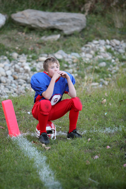 boy sitting on top of a football helmet on the side lines.