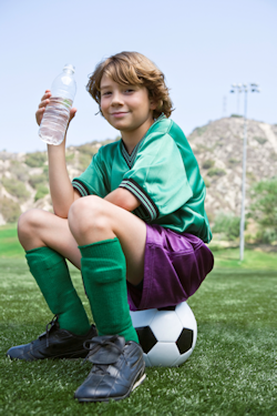 boy sitting on soccerball holding a bottle of water.