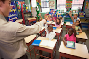 Students in a classroom with their hands raised to answer a question.