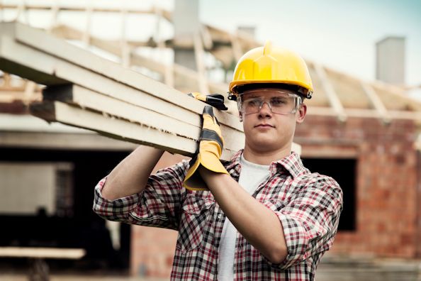 Construction worker carrying wood slats on his shoulder.