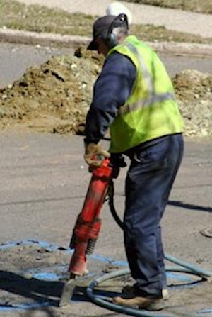 A worker using a jackhammerin the middle of a road.