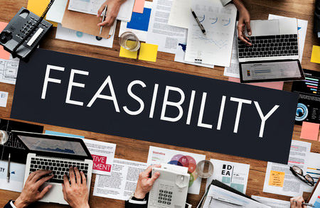 The word feasibility written on a board placed on a table surounded by people using laptop computers.