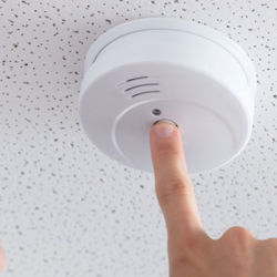 Ceiling mounted fire alarm with a finger pressing the test button