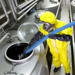 Worker in yellow HAZMAT suit cleaing out a tank with chemicals.