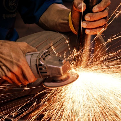 A worker grinding metal with sparks flying around.