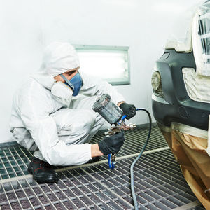 Indoor worker spray painting car and wearing PPE