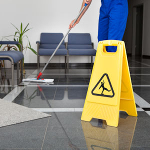 Worker mopping up a wet floor with a self standing caution warning sign .