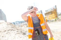 Sweaty worker in an orange vest working in the heat outdoors.