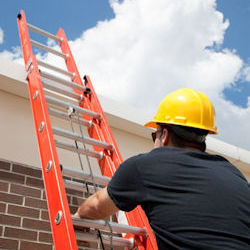 Man with helmet climbing extension ladder.