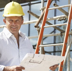 Man wearing helment holding plans standing next to a straight ladder.