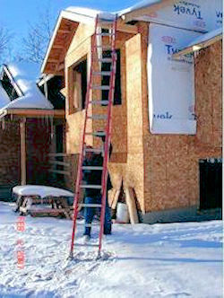  A man is holding a ladder next to a house under construction.