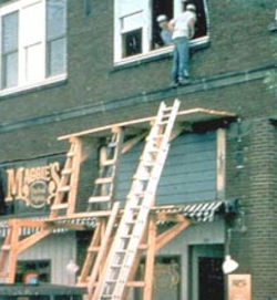 Man climbing through 3rd story window from scaffold that is n