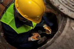 Man climbing down ladder into a sewer.