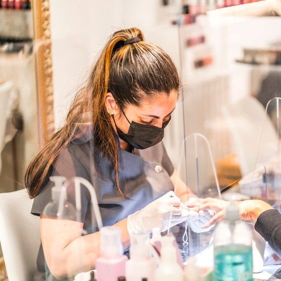 Worker with PPE removing nail polish from client.