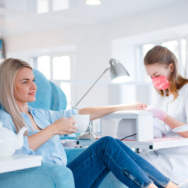 Worker with mask and gloves sitting in chair working on customers hand.