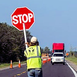 A human flagger wearing the proper safety equipment and holding a STOP sign.