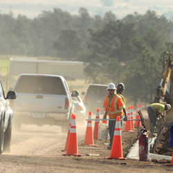 Employees working on a road with cones between them and passing cars.