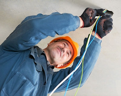 Electrician on ladder working with PPE and electricity in ceiling opening