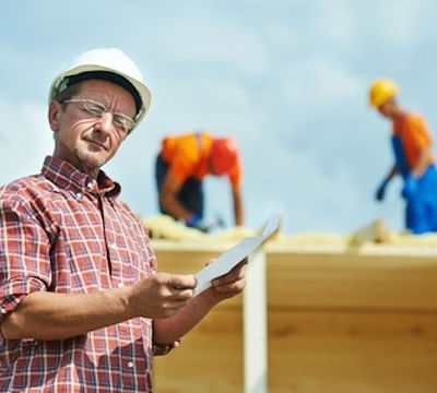 Inspector with PPE and clipboard overseeing two workers on a roof