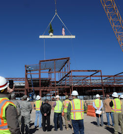 Steel beam being lifted by crane with crowd of workers watching