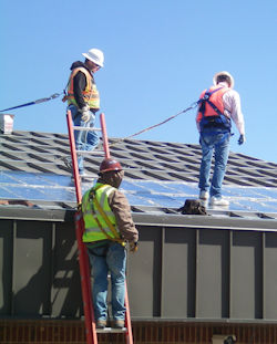 Two workers on a roof and another on a ladder.