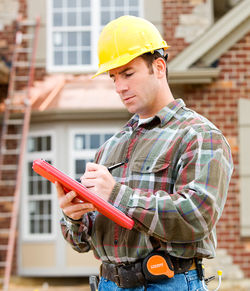 Contractor writing on a clipboard outside of a house being built.