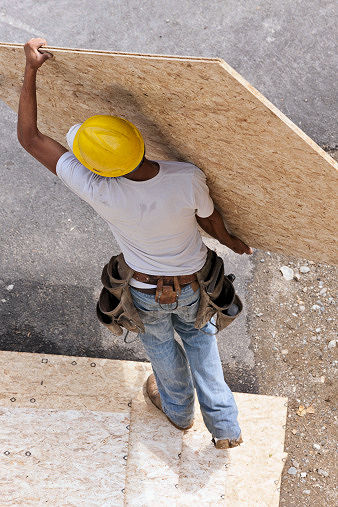 Worker lifting plywood at a construction site.