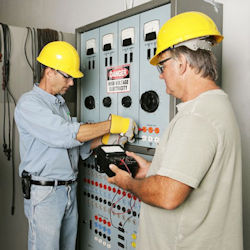 Two electricians testing electrical equipment after LOTO devices have been removed.