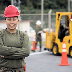 Forklift trainer outdoors wearing hard hat with forklift in background