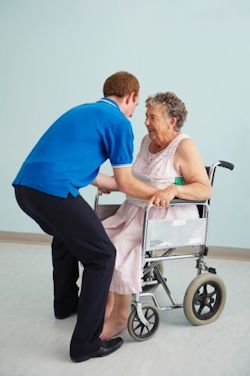 A man helping a patient out of a wheelchair.