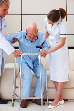 Doctor and nurse assisting an elderly man get up from a couch.