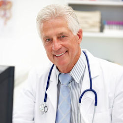 A doctor with a stethoscope around his collar working at a computer.