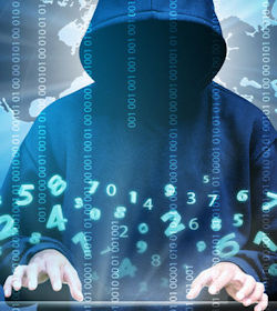 A person in a hooded sweat shirt with the hood covering their face hacking into a computer system.