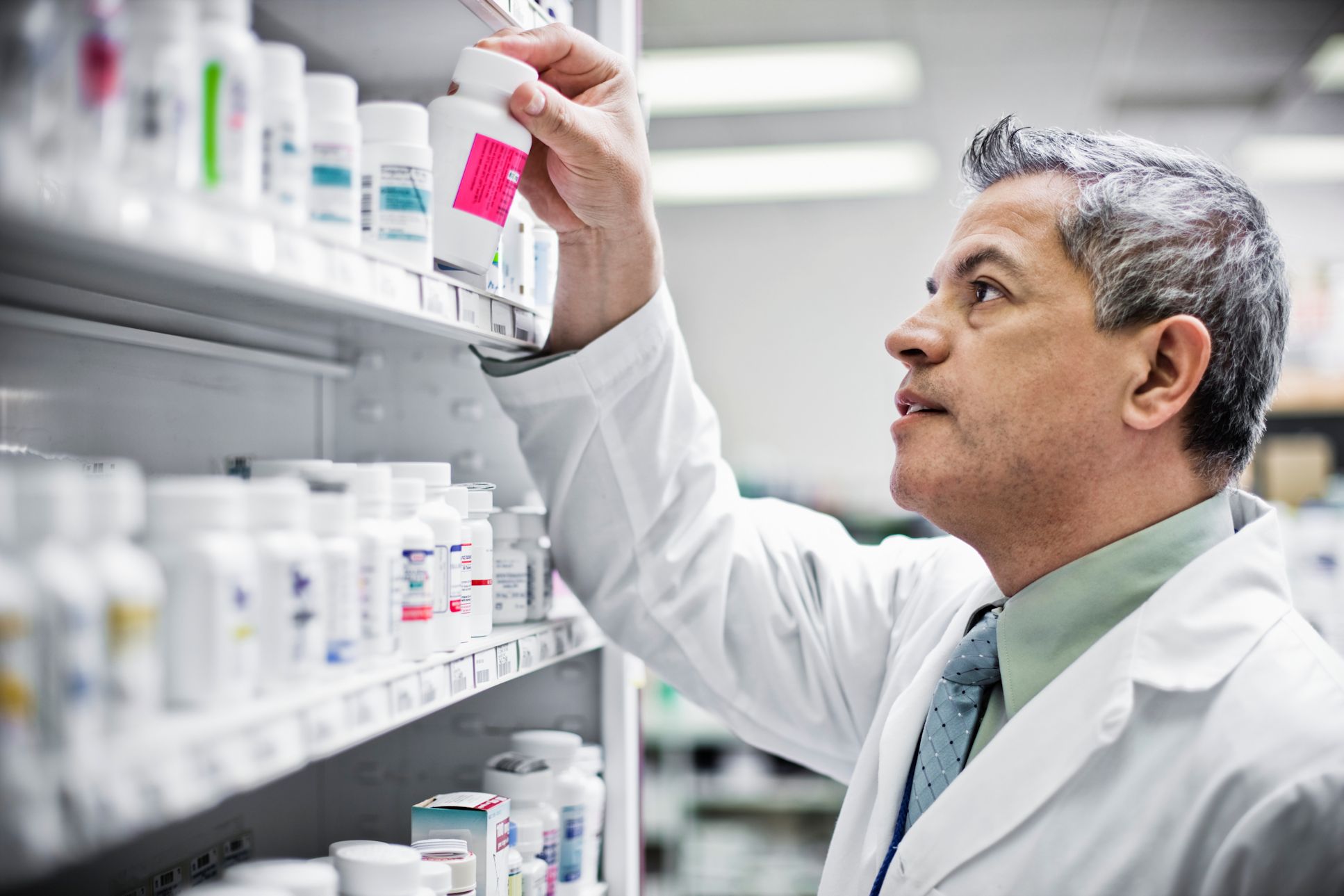 Pharmacist pulling a bottle of pills off of a shelf.