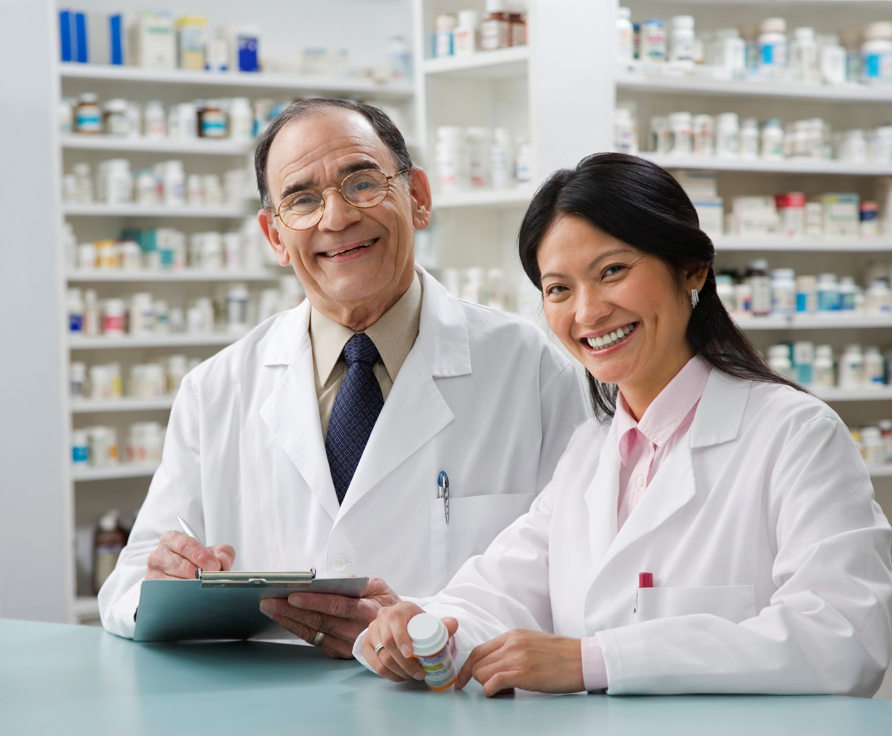 Two pharmacists at the counter and looking at the camera.